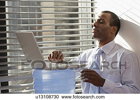 Stock Image - Mid Adult Man Using Laptop on Water Cooler. Fotosearch