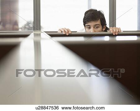 Stock Photograph - Male office worker peeping over partition wall. Fotosearch