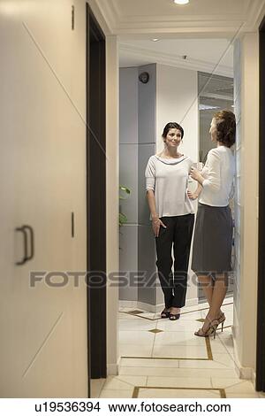 Picture - Two female office workers talking in corridor. Fotosearch