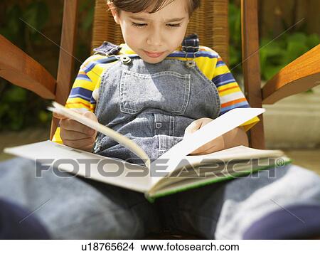 Boy reading book on chair (low angle view) View Large Photo Image Picture - Boy reading book on chair (low angle view). Fotosearch