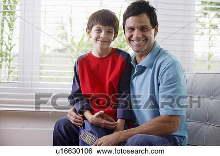 Father and son sitting on armchair, father holding remote control View Large Photo Image Stock Photograph - Father and son sitting on armchair, father holding remote control. Fotosearch