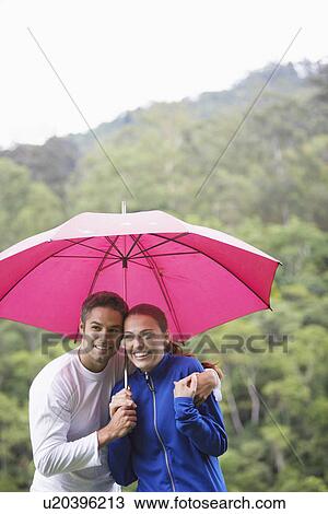 Stock Image - Couple hugging under umbrella. Fotosearch