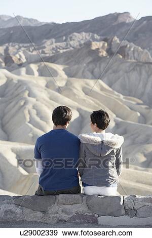 Couple sitting on stone wall in desert (rear view) View Large Photo Image Stock Photo - Couple sitting on stone wall in desert (rear view). Fotosearch