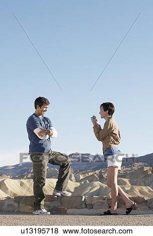 Stock Photo - Woman photographing man by stone wall in desert, Death Valley, California, USA. Fotosearch