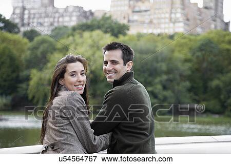 Stock Photo - Young couple looking over shoulder by pond. Fotosearch