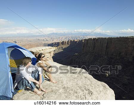 Stock Photograph - Young couple sitting in tent by cliff, high angle view, Moab, Utah, USA. Fotosearch