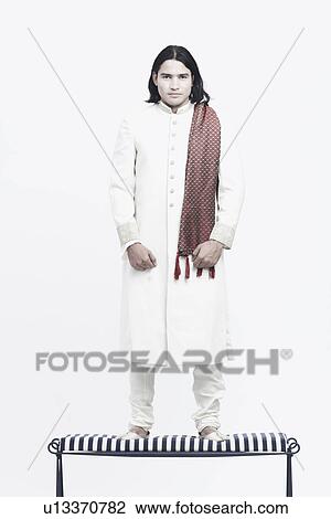 Stock Image - Portrait of a young man in traditional clothing standing on a bench. Fotosearch