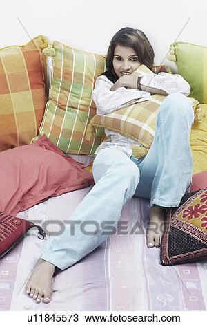 Stock Image - Portrait of a young woman hugging a cushion smiling. Fotosearch