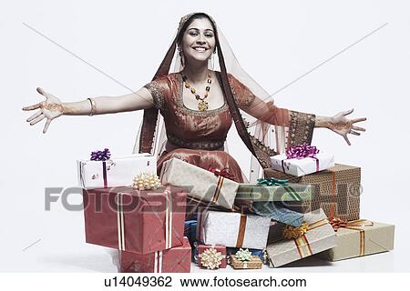Stock Image - Portrait of a young woman smiling with a stack of gifts lying in front of her. Fotosearch