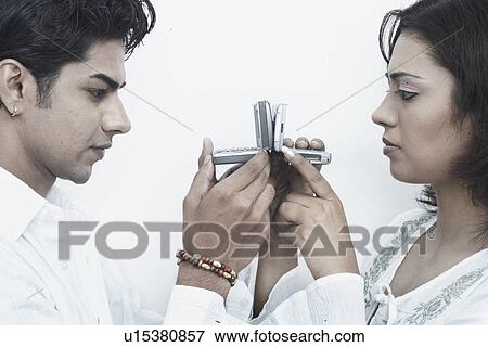 Stock Photo - Side profile of a young couple holding mobile phones in front of their faces. Fotosearch