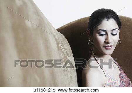 Stock Photography - Side profile of a young woman sitting on a couch. Fotosearch