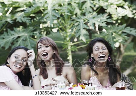 Two young women and a teenage girl sitting at a table and laughing View Large Photo Image Stock Photo - Two young women and a teenage girl sitting at a table and laughing. Fotosearch