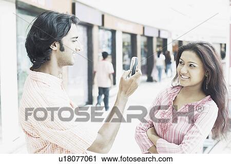 Stock Image - Young man taking a photograph of a young woman. Fotosearch