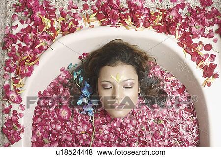 Stock Photo - High angle view of a young woman lying in a bathtub with flower petals floating. Fotosearch