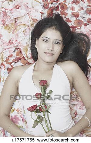 Stock Photography - High angle view of a young woman lying on the bed holding roses. Fotosearch