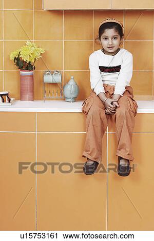 Stock Image - Portrait of a girl sitting on a kitchen counter. Fotosearch