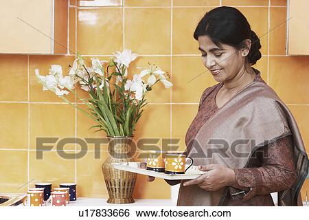 Stock Photograph - Side profile of a mature woman holding a tray with two cups. Fotosearch