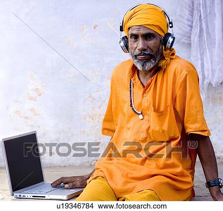 Portrait of a mature man sitting in front of a laptop wearing headphone, Pushkar, Rajasthan, India View Large Photo Image Picture - Portrait of a mature man sitting in front of a laptop wearing headphone, Pushkar, Rajasthan, India. Fotosearch
