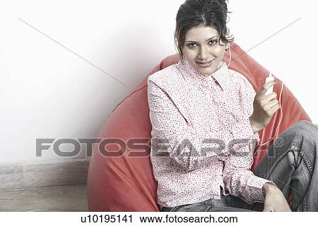 Portrait of a young woman sitting on a couch holding an MP3 Player View Large Photo Image Stock Image - Portrait of a young woman sitting on a couch holding an MP3 Player. Fotosearch