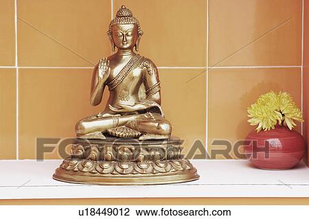 Stock Image - Close-up of a statue of Buddha and a flower vase. Fotosearch
