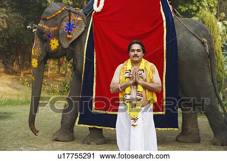 Stock Image - Priest standing in a prayer position beside an elephant. Fotosearch