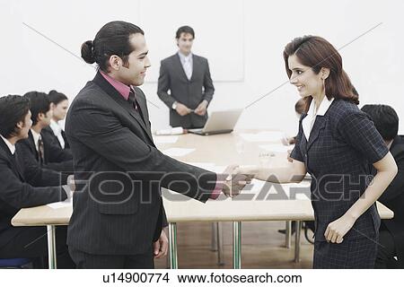 Picture - Side profile of a businessman and a businesswoman shaking hands in a meeting. Fotosearch