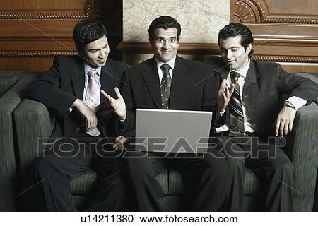 Three businessmen sitting on a couch with a laptop View Large Photo Image Stock Image - Three businessmen sitting on a couch with a laptop. Fotosearch