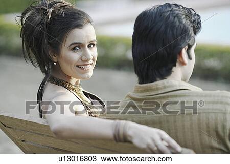Stock Image - Close-up of a young couple sitting on a bench. Fotosearch