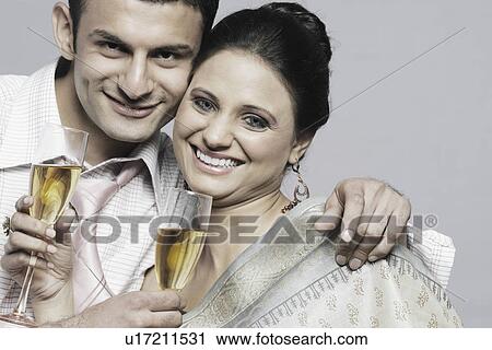 Stock Image - Portrait of a young couple holding champagne flutes. Fotosearch