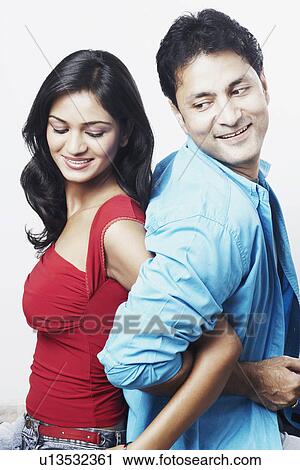 Stock Image - Side profile of a young couple standing back to back. Fotosearch