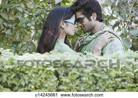 Side profile of a young couple standing behind a hedge View Large Photo Image Stock Image - Side profile of a young couple standing behind a hedge. Fotosearch