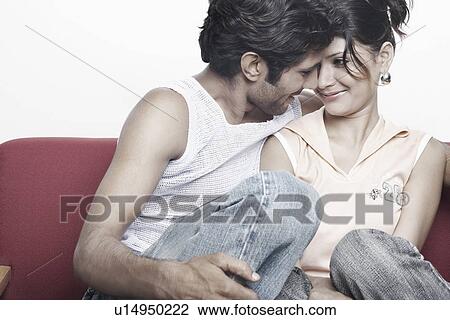 Young couple sitting on a couch looking at each other View Large Photo Image Stock Image - Young couple sitting on a couch looking at each other. Fotosearch