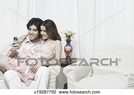 Close-up of a young woman sitting on a young man's lap looking at a mobile phone View Large Photo Image Stock Image - Close-up of a young woman sitting on a young man's lap looking at a mobile phone. Fotosearch