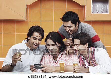 Stock Image - Close-up of four young men looking at a mobile phone. Fotosearch