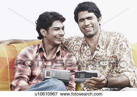 Stock Photo - Close-up of two young men holding mobile phones and smiling. Fotosearch