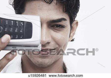 Portrait of a young man holding a mobile phone in front of his face View Large Photo Image Stock Image - Portrait of a young man holding a mobile phone in front of his face. Fotosearch