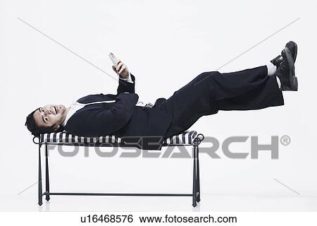 Portrait of a young man lying on the table operating a mobile phone View Large Photo Image Stock Photograph - Portrait of a young man lying on the table operating a mobile phone. Fotosearch