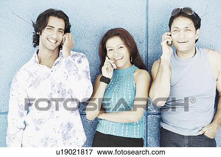 Stock Photo - Young woman with two young men talking on mobile phones. Fotosearch