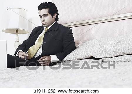 Stock Image - Low angle view of a businessman sitting on the bed. Fotosearch