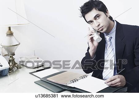 Portrait of a businessman sitting in an office talking on the telephone View Large Photo Image Stock Image - Portrait of a businessman sitting in an office talking on the telephone. Fotosearch