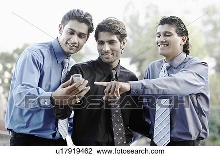 Stock Image - Three businessmen looking at a mobile phone. Fotosearch