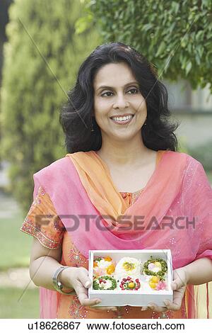 Stock Photo - Portrait of a mid adult woman holding a box of Indian sweets. Fotosearch
