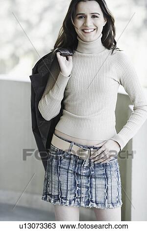 Stock Image - Portrait of a young woman holding a jacket over her shoulder. Fotosearch