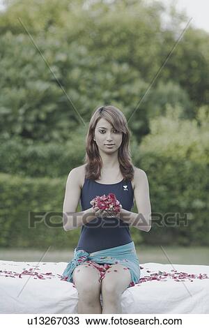 Stock Image - Portrait of a young woman holding rose petals in her palm. Fotosearch