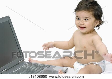 Stock Image - Close-up of a baby boy sitting in front of a laptop. Fotosearch