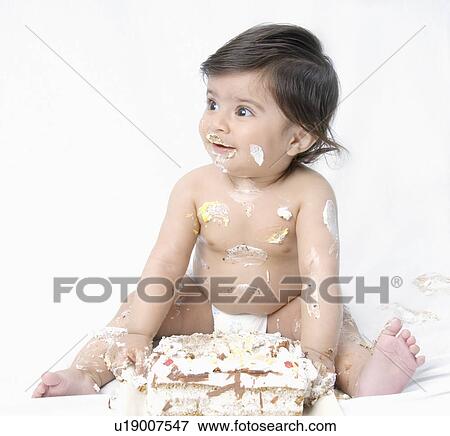Stock Photo - Close-up of a baby boy sitting in front of a cake with icing on his body. Fotosearch