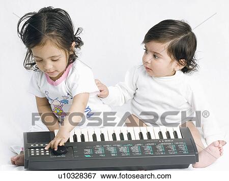 Close-up of a baby girl playing an electronic piano with her brother sitting beside her View Large Photo Image Stock Photo - Close-up of a baby girl playing an electronic piano with her brother sitting beside her. Fotosearch