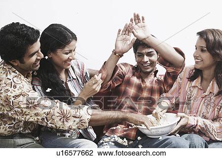 Close-up of two young couples sitting together on a couch eating popcorn View Large Photo Image Stock Image - Close-up of two young couples sitting together on a couch eating popcorn. Fotosearch