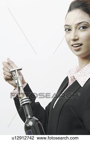 Stock Image - Portrait of a businesswoman opening a champagne bottle. Fotosearch