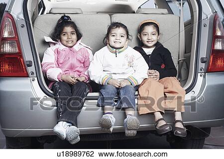 Stock Image - Portrait of three sisters sitting in the back of a car. Fotosearch